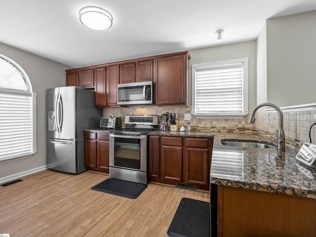 kitchen featuring visible vents, light wood finished floors, a sink, decorative backsplash, and stainless steel appliances