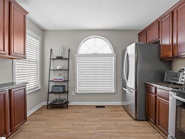 kitchen with dark stone countertops, baseboards, a toaster, stainless steel appliances, and light wood-style floors