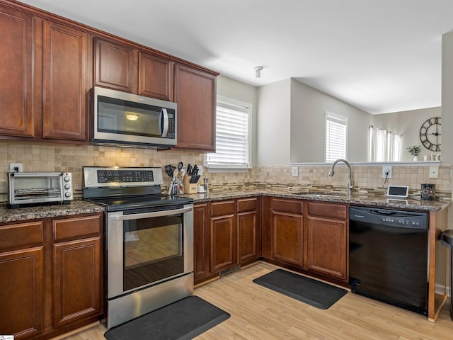 kitchen featuring dark stone countertops, a toaster, a sink, stainless steel appliances, and tasteful backsplash