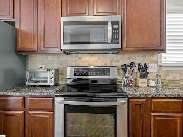 kitchen with stainless steel appliances, dark stone counters, decorative backsplash, and a toaster