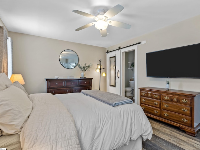 bedroom featuring ensuite bath, a barn door, wood finished floors, and a ceiling fan