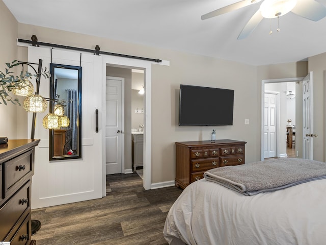 bedroom featuring a barn door, baseboards, dark wood finished floors, and ensuite bathroom