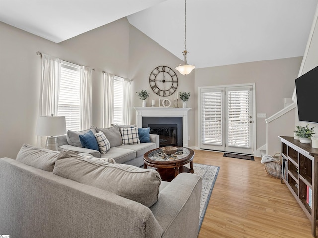 living room with a glass covered fireplace, light wood-style floors, baseboards, and high vaulted ceiling