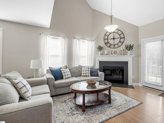 living room with baseboards, a fireplace with flush hearth, high vaulted ceiling, and wood finished floors