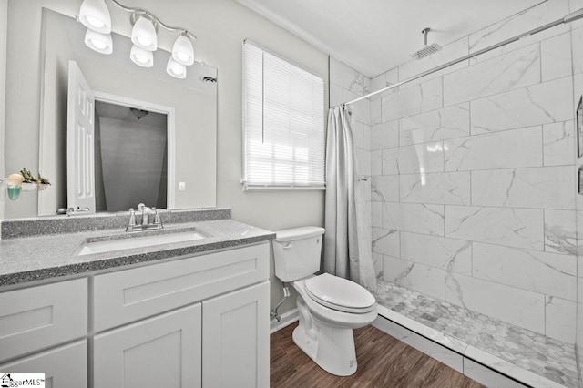 bathroom with a tile shower, toilet, vanity, and wood finished floors