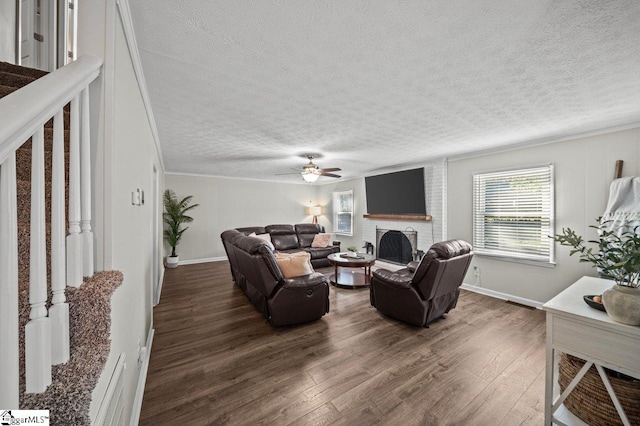 living area featuring baseboards, dark wood finished floors, ceiling fan, a textured ceiling, and a brick fireplace