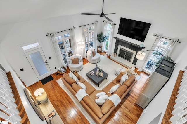 living room with a glass covered fireplace, lofted ceiling, a ceiling fan, and wood finished floors