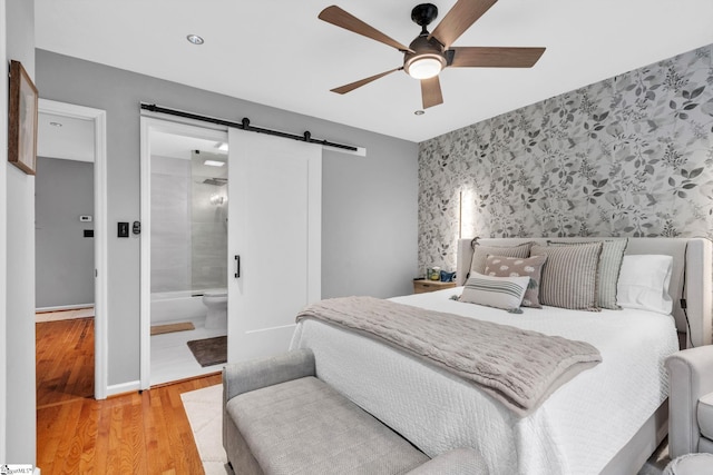 bedroom featuring wallpapered walls, an accent wall, baseboards, a barn door, and wood finished floors