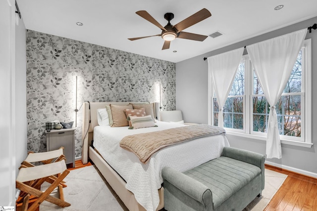 bedroom featuring visible vents, baseboards, wallpapered walls, an accent wall, and light wood-type flooring