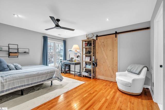 bedroom featuring a barn door, light wood-style floors, and a ceiling fan