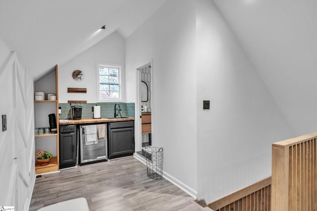 bar with light wood-style flooring, a sink, wine cooler, decorative backsplash, and lofted ceiling