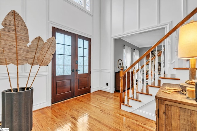 entrance foyer with stairway, light wood-style floors, french doors, crown molding, and a decorative wall
