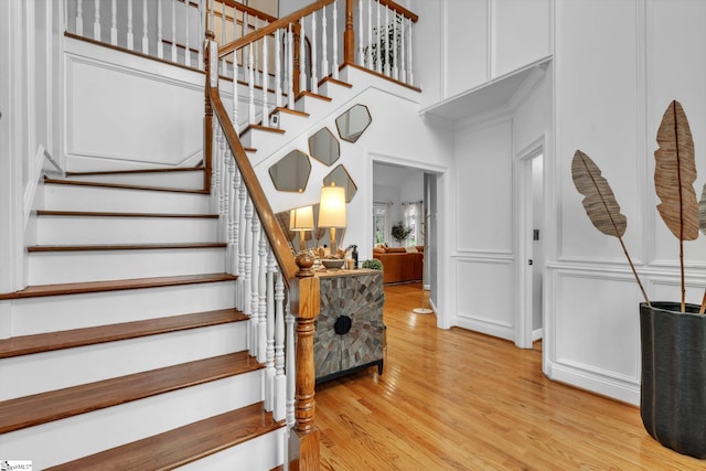stairs featuring a decorative wall, wood finished floors, and a high ceiling