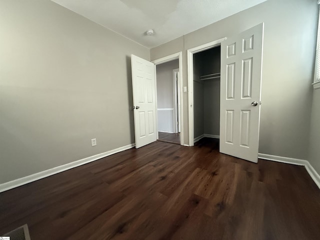 unfurnished bedroom featuring visible vents, baseboards, a closet, and dark wood-style flooring