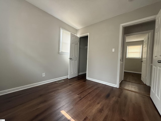 unfurnished bedroom with dark wood-type flooring, baseboards, visible vents, and a closet