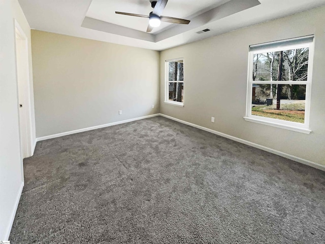 empty room with visible vents, baseboards, carpet, a tray ceiling, and a ceiling fan