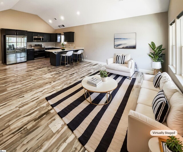 living area with light wood-style flooring, baseboards, and vaulted ceiling