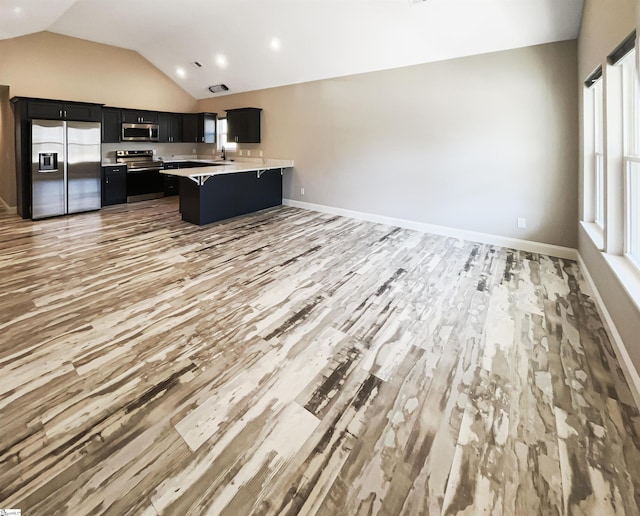 kitchen featuring open floor plan, a peninsula, appliances with stainless steel finishes, light countertops, and dark cabinets