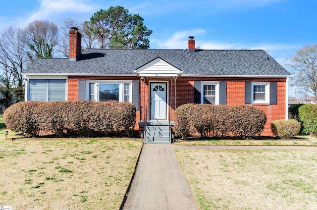 view of front of house featuring brick siding, a chimney, a front yard, and roof with shingles