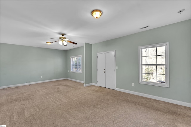 empty room with carpet, a ceiling fan, visible vents, and baseboards