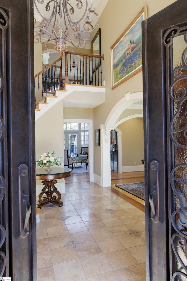 foyer entrance featuring stairway, arched walkways, a high ceiling, an inviting chandelier, and baseboards