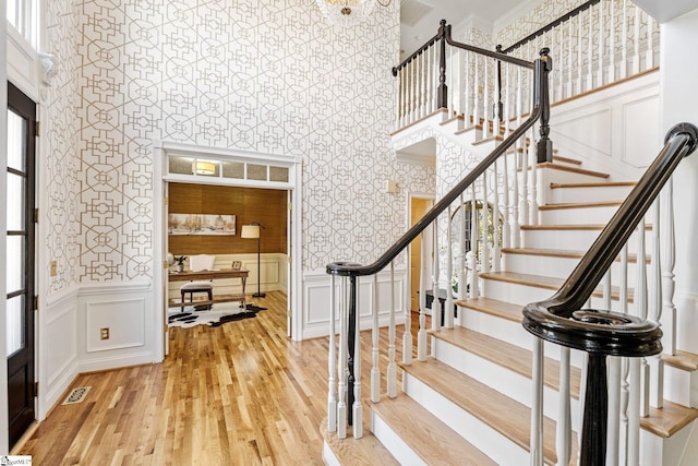 stairway with wallpapered walls, a decorative wall, wood finished floors, and visible vents