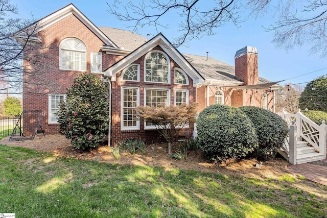 rear view of property with brick siding, a lawn, a chimney, and fence