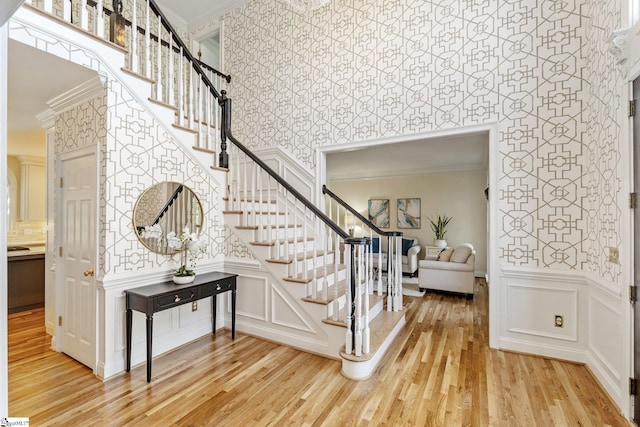 stairs with wallpapered walls, crown molding, and wood finished floors