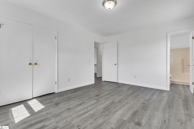 unfurnished bedroom featuring ensuite bath, baseboards, and wood finished floors