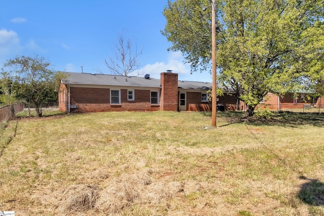 rear view of property with a yard, fence, brick siding, and a chimney