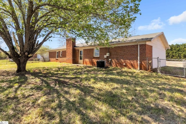 back of property featuring fence, a yard, brick siding, central AC unit, and a chimney