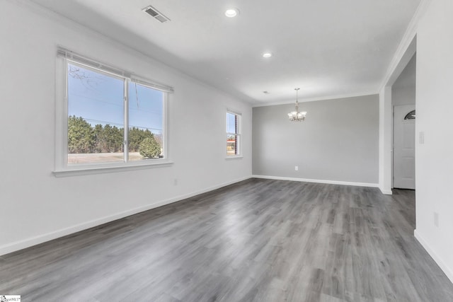 empty room featuring wood finished floors, visible vents, baseboards, crown molding, and a chandelier