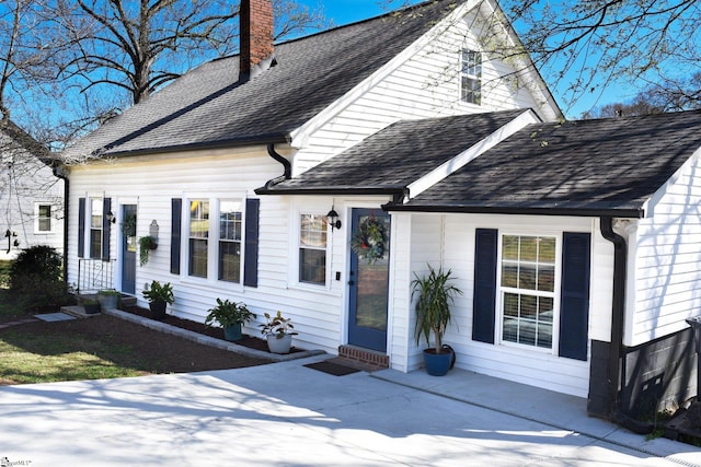 cape cod house featuring entry steps, a chimney, and a shingled roof