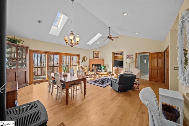dining space featuring heating unit, ceiling fan with notable chandelier, light wood-style flooring, and a skylight