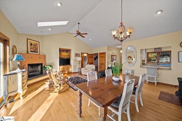 dining area with vaulted ceiling with skylight, plenty of natural light, a fireplace with raised hearth, and light wood-style floors