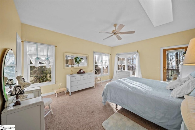 carpeted bedroom featuring multiple windows, a skylight, baseboards, and a ceiling fan