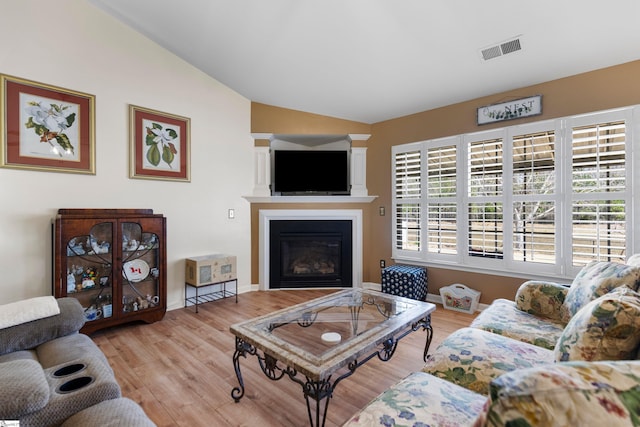 living room featuring a glass covered fireplace, vaulted ceiling, wood finished floors, and visible vents