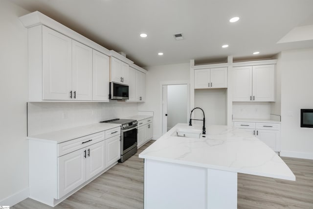 kitchen featuring visible vents, an island with sink, a sink, backsplash, and stainless steel appliances