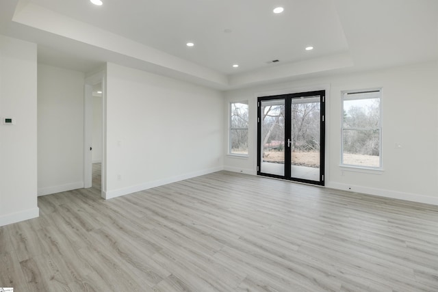 empty room with recessed lighting, a tray ceiling, baseboards, and light wood-style flooring