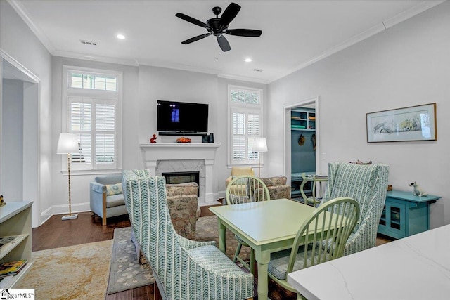dining space featuring a ceiling fan, a fireplace, wood finished floors, visible vents, and ornamental molding