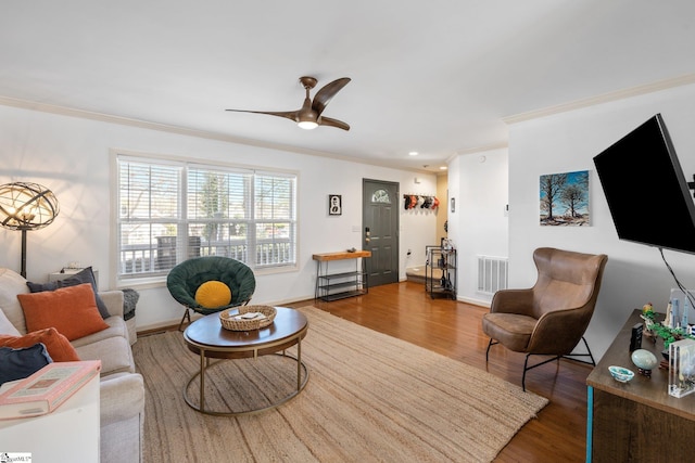living area with ceiling fan, visible vents, wood finished floors, and ornamental molding