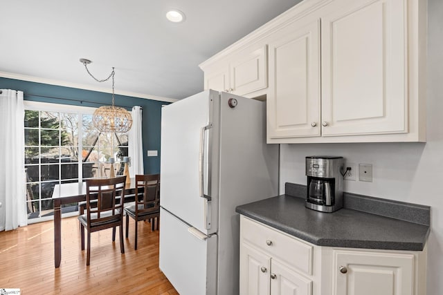 kitchen with an inviting chandelier, freestanding refrigerator, white cabinetry, dark countertops, and light wood-type flooring