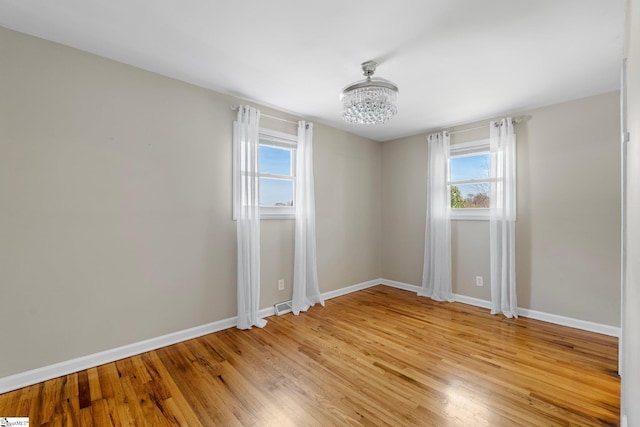 unfurnished room with baseboards, light wood-style floors, and a chandelier
