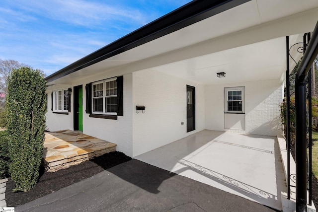 entrance to property featuring a patio area, an attached carport, and brick siding