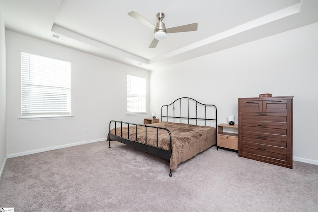 carpeted bedroom with a tray ceiling, baseboards, visible vents, and ceiling fan