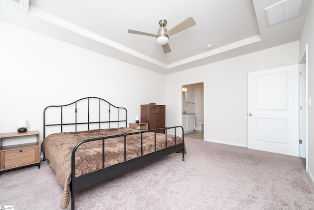 bedroom featuring baseboards, visible vents, ensuite bath, a tray ceiling, and light carpet