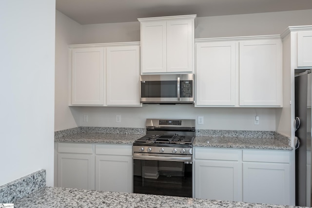 kitchen with white cabinetry, stainless steel appliances, and light stone countertops