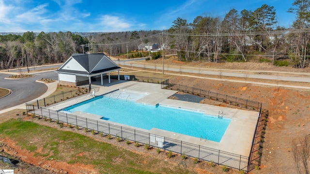 community pool featuring a view of trees, a patio, and fence