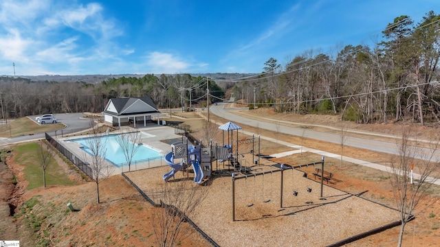 community pool featuring a forest view, playground community, and fence