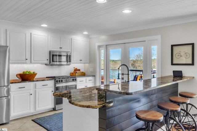 kitchen featuring a breakfast bar, dark stone countertops, stainless steel appliances, light tile patterned floors, and decorative backsplash
